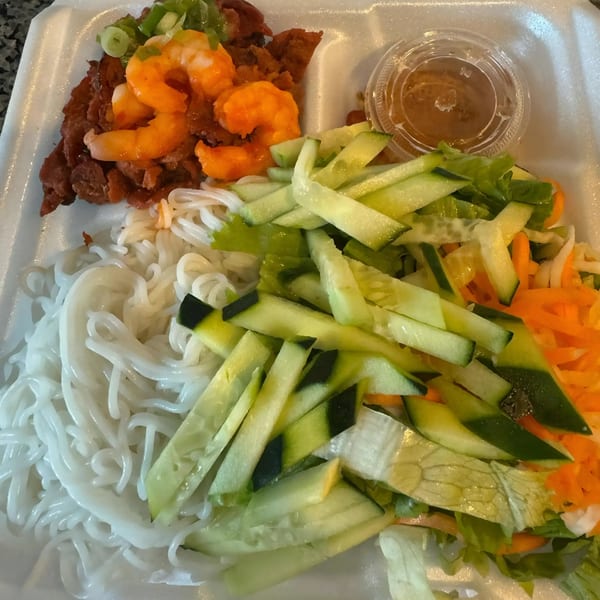 Vietnamese vermicelli bowl with shrimp, pork, vegetables, and a side of sauce in a takeout container.
