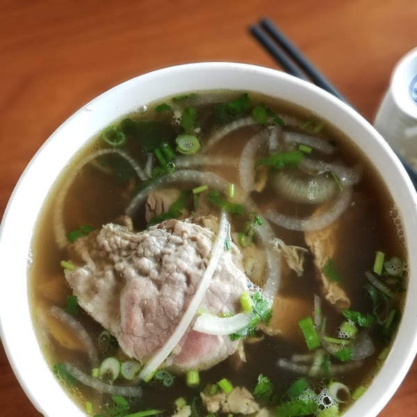 Close-up of a bowl of Vietnamese pho with beef, onions, and green herbs.