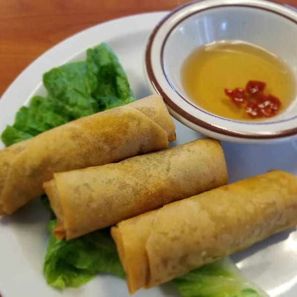 Three golden-brown Vietnamese egg rolls on lettuce with a side of dipping sauce.