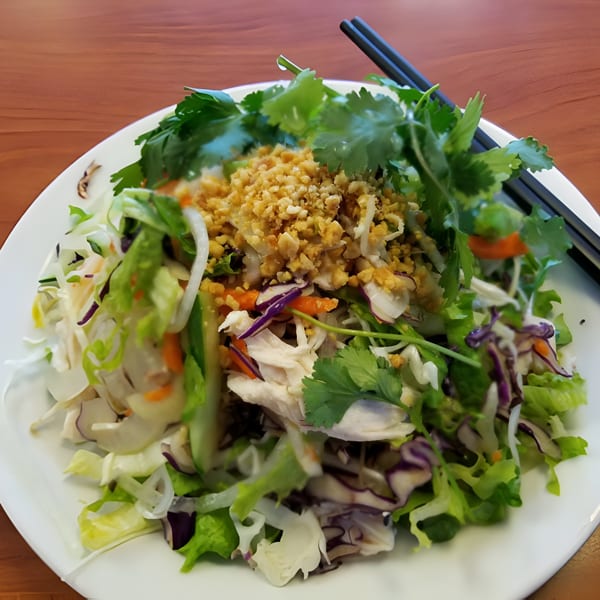 Vietnamese chicken salad with shredded cabbage, carrots, cilantro, and crushed peanuts on a white plate.