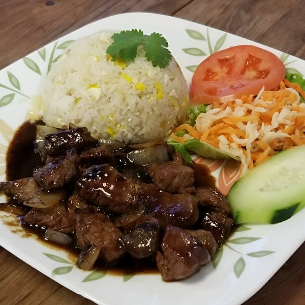 Vietnamese shaking beef (Bo Luc Lac) with fried rice, tomato, cucumber, and pickled carrots on a white plate.