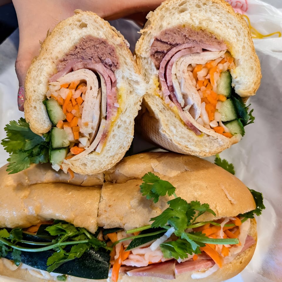 Two Vietnamese banh mi sandwiches, one cut in half, revealing meats, pickled vegetables, and cilantro.