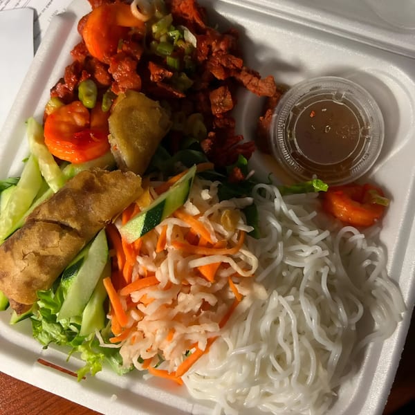 Vietnamese vermicelli bowl with red meat, spring roll, pickled vegetables, and sauce in a takeout container.